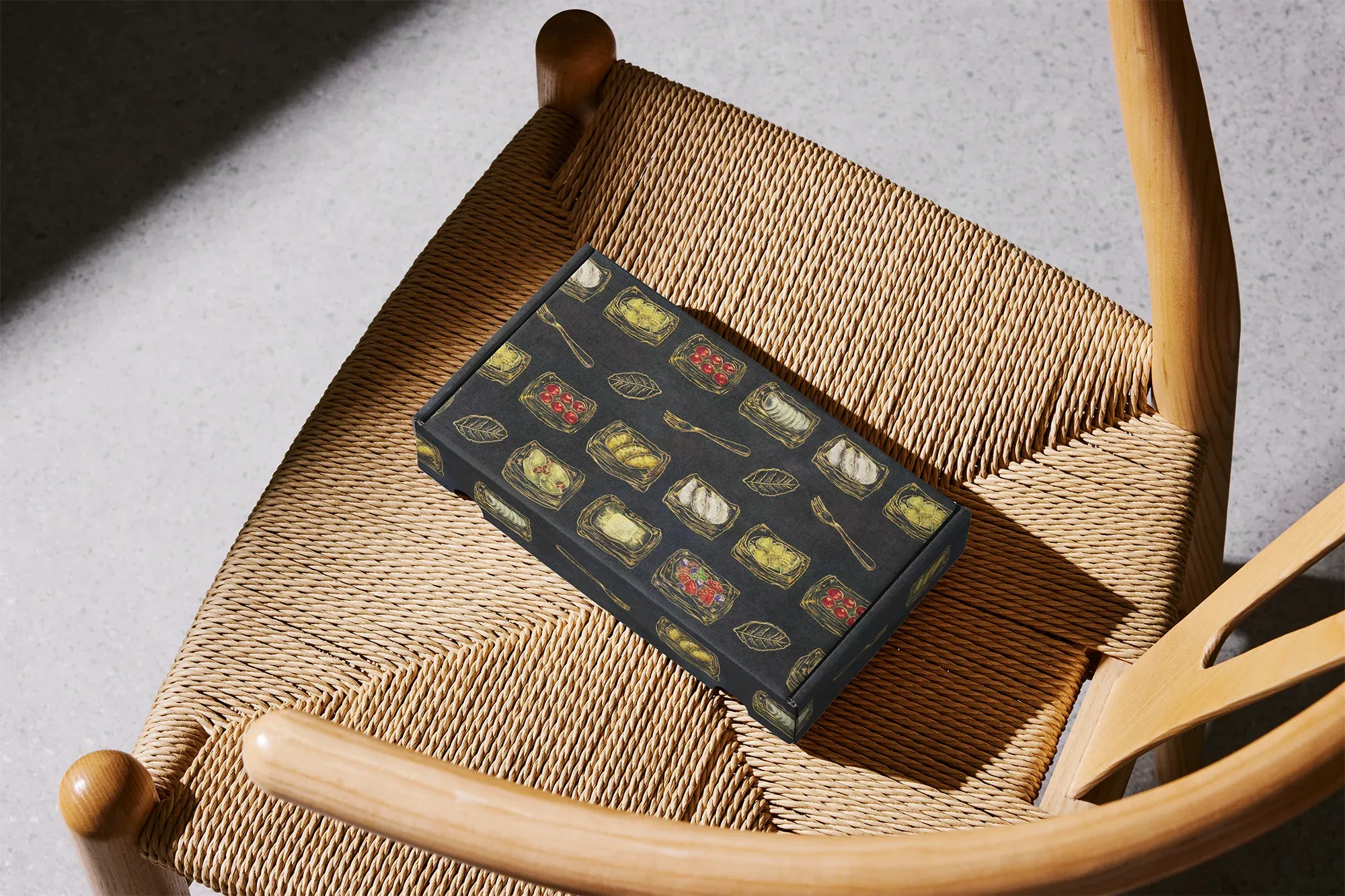木製の椅子の上に置かれた、様々なデニッシュがデザインされた黒い箱。