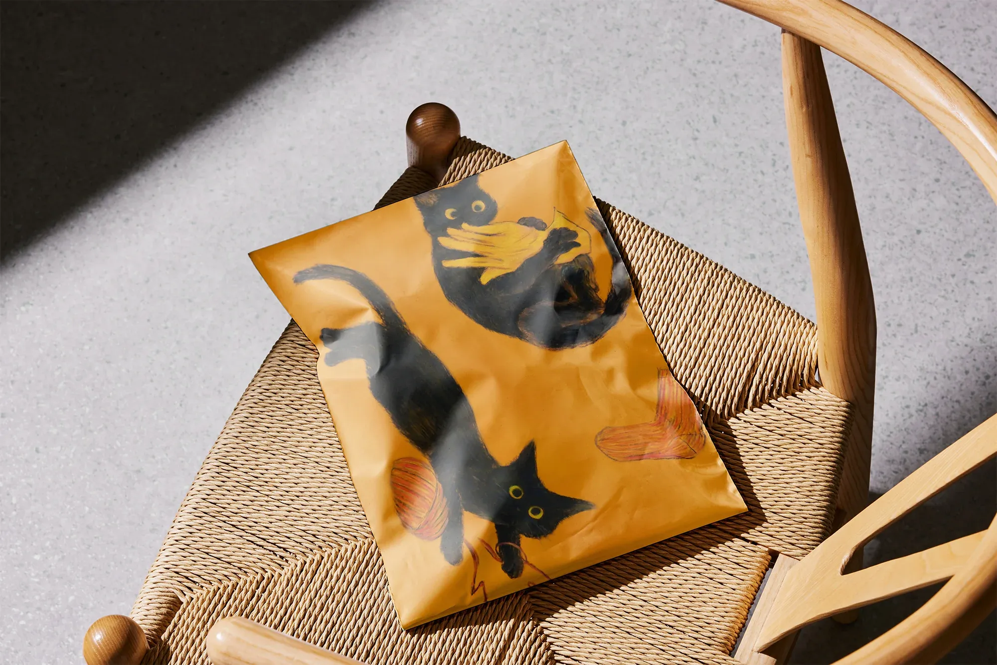 木製の椅子の上に置かれた、黒猫と毛糸玉が描かれたオレンジの紙パッケージ。