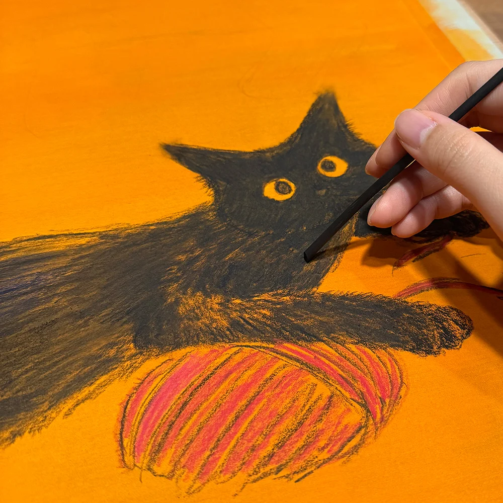 炭で毛糸玉とじゃれる黒猫をオレンジ色の背景に描く様子